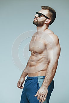 .bodybuilder posing. Beautiful sporty guy male power. Fitness muscled in blue shorts and sunglasses. on isolated grey