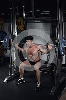 Bodybuilder squatting with a barbell. Bodybuilder working with barbell. Fitness man doing squats with the barbell at the gym. Smit