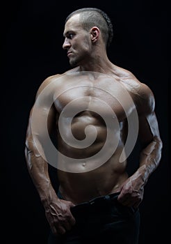 Bodybuilder and strip theme: beautiful with pumped muscles naked man posing in the studio on a dark background