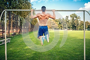 bodybuilder working out in park, doing chin ups and push ups. Male fitness player training outdoors