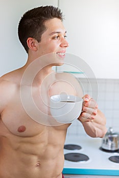 Bodybuilder young man daydreaming future shirtless drinking coffee in the kitchen portrait format