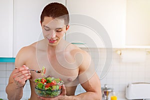 Bodybuilder young man eating salad in the kitchen copyspace heal