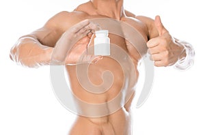 Bodybuilding and chemical additives: handsome strong bodybuilder holding a white jar of pills on white isolated background in stud