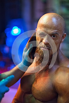 Bodybuilding competition backstage: contestant being oiled and fake tan applied to skin