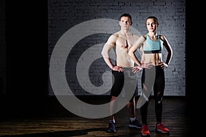 Bodybuilding. Strong man and a woman posing on a brick wall background.