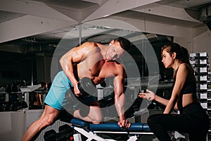 Bodybuiler couple trainig biceps. Personal trainer helping woman working with heavy dumbbells in gym. Sportsman concept