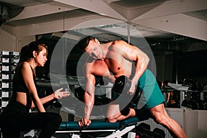 Bodybuiler couple trainig biceps. Personal trainer helping woman working with heavy dumbbells in gym. Sportsman concept