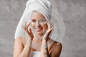 Bodycare concept. Portrait of beautiful young lady with cream on cheeks and white towel on head smiling at camera