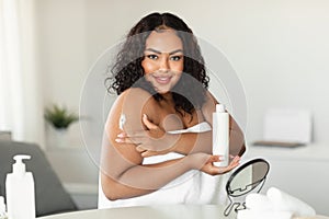 Bodycare and skin nutrition. Happy african american plus size lady using body lotion, doing daily morning routine