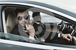 bodyguard in sunglasses talking by portable radio while sitting