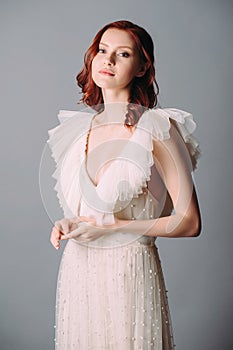 Bohemian wedding, elegant bridal look. Beautiful ginger bride in white wedding dress with sexy decollete and frills on grey backgr photo