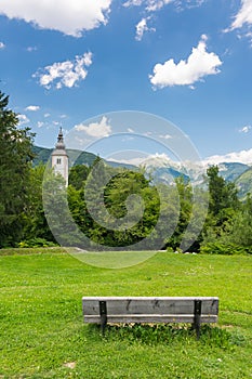 Bohinj church in the Ribcev Laz village, Slovenia. View of old ancient church from the park with bench. Slovenia alps with Triglav