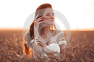 Boho chic style. Portrait of bohemian girl with white art posing over wheat field enjoying at sunset. Outdoors photo. Tranquility