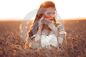 Boho chic style. Portrait of bohemian girl with white art posing over wheat field enjoying at sunset. Outdoors photo. Tranquility