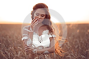 Boho chic style. Portrait of bohemian girl with white art posing over wheat field enjoying at sunset. Outdoors photo. Tranquility