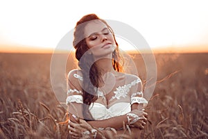 Boho chic style. Portrait of bohemian girl with white art posing over wheat field enjoying at sunset. Outdoors photo. Tranquility photo