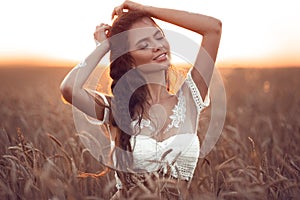 Boho chic style. Portrait of bohemian girl with white art posing over wheat field enjoying at sunset. Outdoors photo. Tranquility