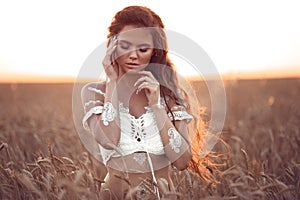 Boho chic style. Portrait of bohemian girl with white art posing over wheat field enjoying at sunset. Outdoors photo. Tranquility