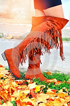 Boho girl walking in knee-high fringe boots on the autumn day