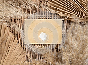 Boho sealed envelope on a wattled table with dry palm leaves and pampas grass