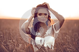 Boho style portrait of bohemian girl with white art posing over wheat field at sunset. Outdoors photo. Tranquility concept