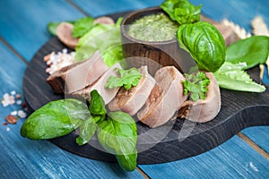 Boiled beef tongue on dark wooden table with pesto