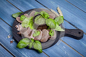 Boiled beef tongue on dark wooden table with pesto