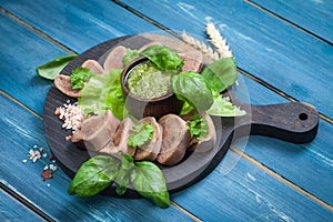 Boiled beef tongue on dark wooden table with pesto and salad