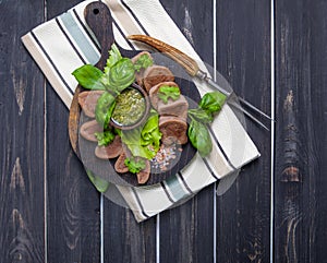 Boiled beef tongue on dark wooden table with pesto and salad
