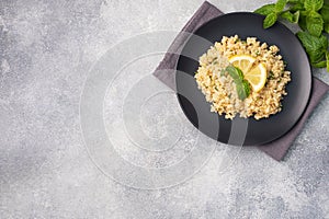 Boiled bulgur with fresh lemon and mint on a plate. A traditional oriental dish called Tabouleh. Gray concrete background top view