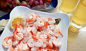 Boiled Caridean Shrimp served with sliced fresh lemon. Two glasses with cold white wine. Red grapes for dessert