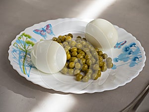 Boiled chicken eggs and canned green peas for easy quick breakfast on a white ceramic plate