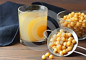 Boiled chickpea water - aquafaba with beans and blue napkin on wooden table nearby