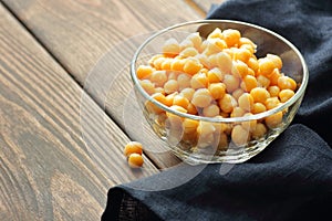 Boiled chickpeas in a glass bowl on rustic wooden table with blue cloth