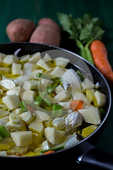 Boiled cod with potatoes, celery and carrots. Close-up of pan ready to cook, on green wooden background