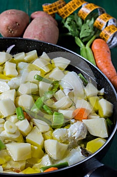Boiled cod with potatoes, celery and carrots. Close-up of pan ready to cook, on green wooden background