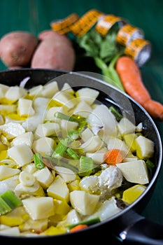 Boiled cod with potatoes, celery and carrots. Close-up of pan ready to cook, on green wooden background