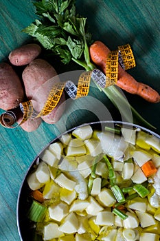 Boiled cod with potatoes, celery and carrots. Close-up of pan ready to cook, on green wooden background