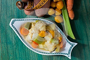 Boiled cod with potatoes, celery and carrots. Close-up of plate ready to cook, on green wooden background