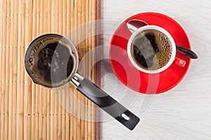 Boiled coffee in cezve on mat, coffee in cup, spoon