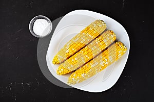 boiled corn on a white square plate, dark table, hodgepodge with salt. photo