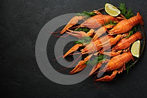 Boiled Crayfish on black plate on dark slate table top. Red crawfish with green dill and lime is popular party dish