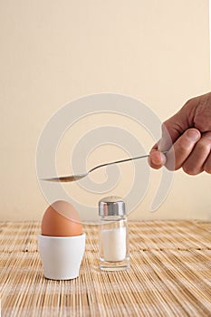 Boiled egg in an egg cup and a man`s hand holding a spoon