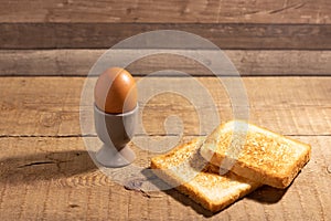 Boiled egg in an egg cup with a slice of fried toast bread on a natural brown wooden background.