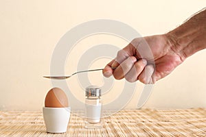 Boiled egg in an egg cup and a man`s hand holding a spoon