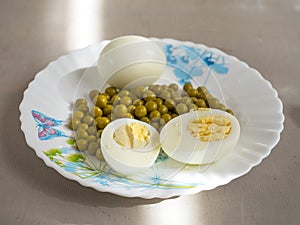 Boiled eggs and canned green peas on a light plate for a diet breakfast close-up