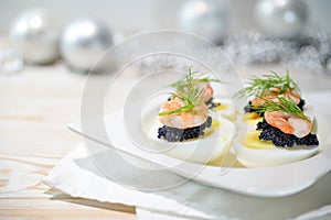 Boiled eggs with caviar and shrimps, garnished with dill on a white plate, festive decoration blurred in the background, holiday