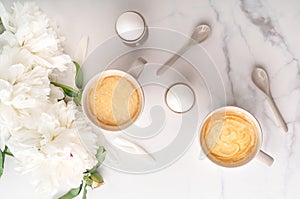 Boiled eggs in ceramic egg cups and two cups of coffee on background of beautiful white peony. Breakfast concept. Top view