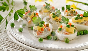 Boiled eggs divided into halves filled with vegetable and mayonnaise salad served on a white plate.