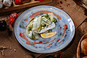 Boiled fish covered with fresh cucumber on a plate. Top view